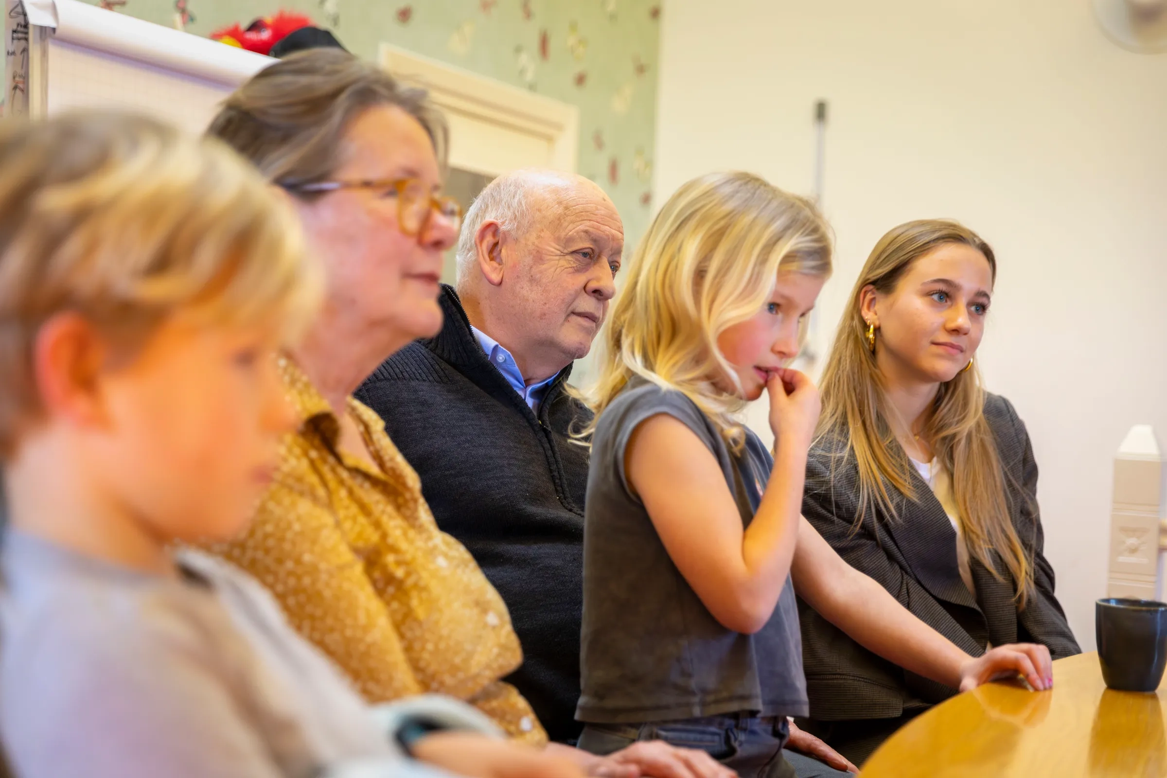 Grootouders, kinderen en jongere zitten samen aan tafel tijdens gezinsgesprek