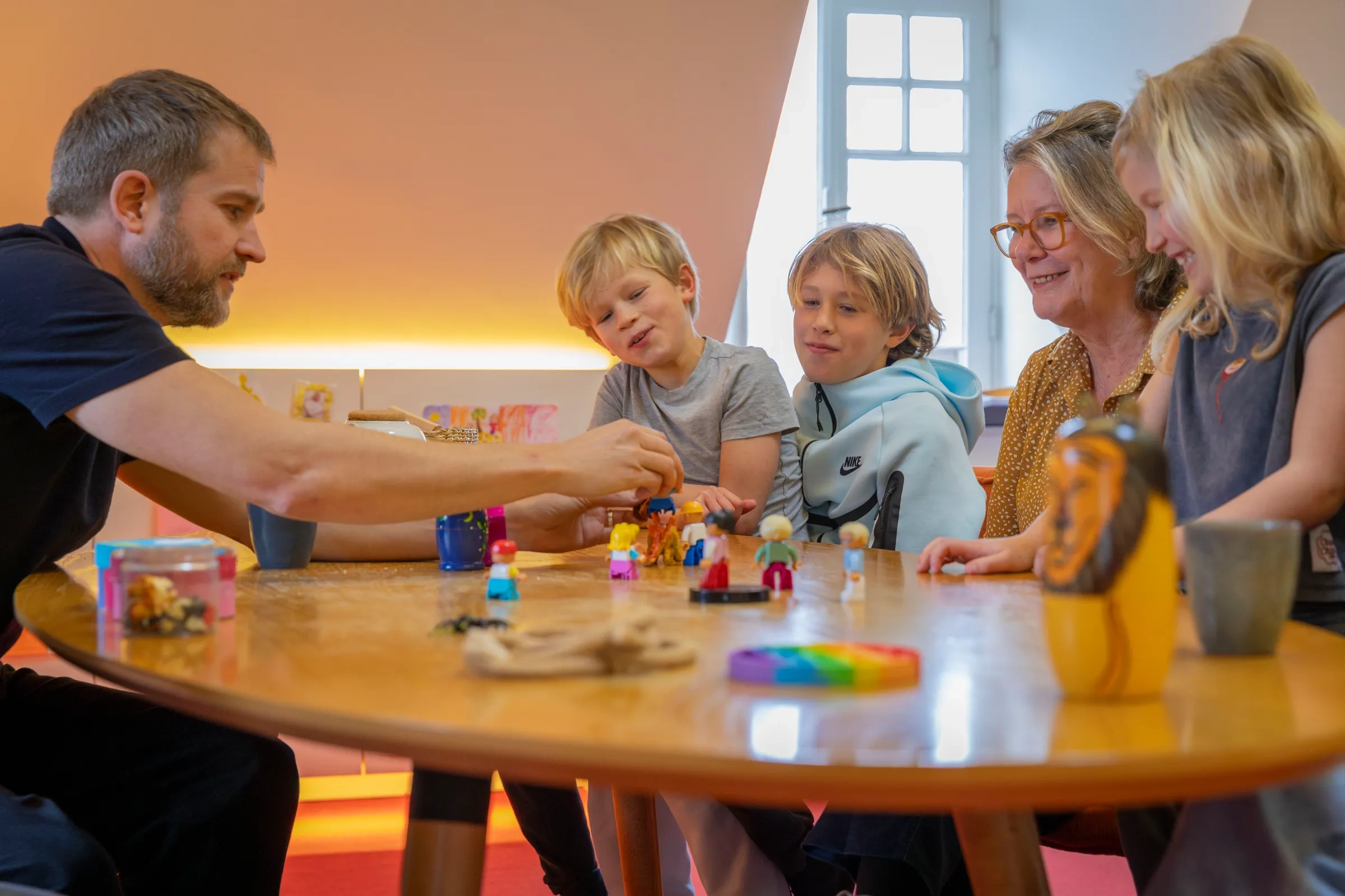 Vader en kinderen spelen met poppetjes aan de tafel terwijl oma meekijkt